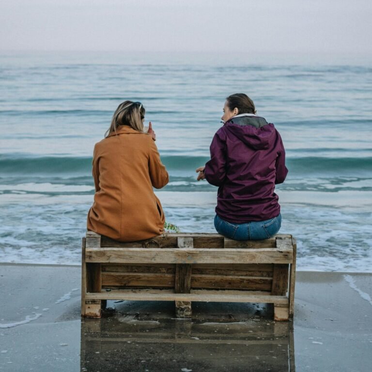 Two women sitting on a pallet by the Odesa shoreline, enjoying the serene sea view.