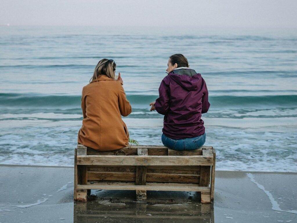 Two women sitting on a pallet by the Odesa shoreline, enjoying the serene sea view.